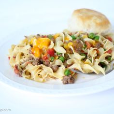 a white plate topped with pasta and veggies next to a roll on a table