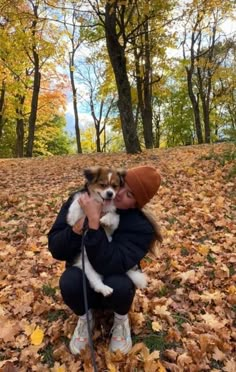 a woman is holding a small dog in her lap while sitting on the ground covered with leaves