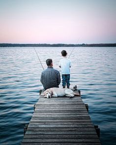 a father and son sitting on a dock with their dog fishing in the water at sunset