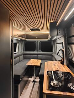 the interior of a camper with wood flooring and black couches, stove top oven