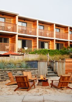 three wooden chairs sitting on top of a sandy beach next to an apartment building with balconies