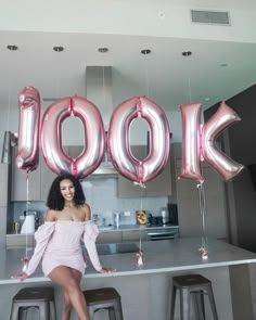 a woman sitting on top of a counter next to giant balloons that spell out look