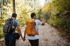 two men walking down a dirt road in the woods with backpacks on their backs