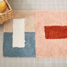 a bathroom rug on the floor next to a basket with an orange and blue object