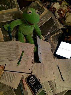 a stuffed frog sitting on top of a pile of papers next to a cell phone