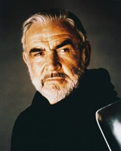 an older man with white hair and beard wearing a black shirt is looking at the camera