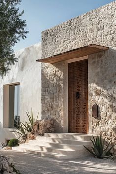 a stone building with a wooden door next to some plants and rocks on the ground