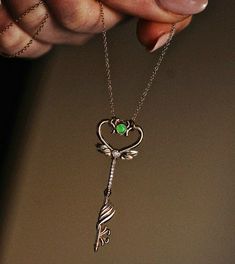 a woman's hand holding a silver necklace with a green crystal key attached to it