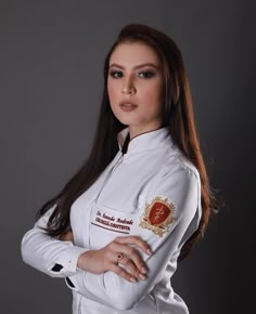 a woman with long hair wearing a white jacket and posing for a photo in front of a gray background