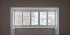 an empty room with white walls and wooden shutters on the windowsill, in front of a cityscape