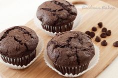 three chocolate muffins sitting on top of a wooden cutting board