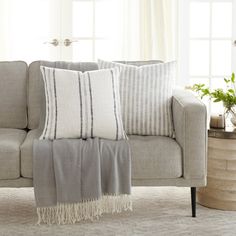 a living room with a gray couch and white pillows on the armrests, along with a potted plant