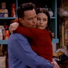 the young man and woman are hugging each other in front of shelves with books on them