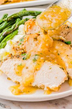 a white plate topped with chicken and asparagus covered in gravy next to a fork