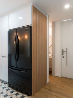 a black refrigerator freezer sitting inside of a kitchen next to a white wall and wooden floor