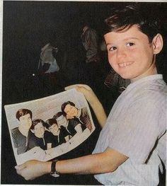 a young boy holding up a newspaper with pictures on it