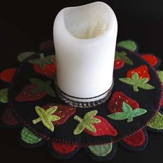 a white candle sitting on top of a black placemat with strawberries and leaves