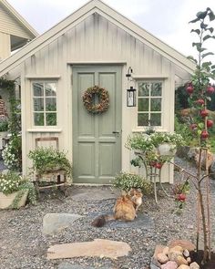 a cat sitting in front of a small house with a wreath on it's door