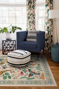 a blue chair and ottoman in front of a window with floral curtains on the windowsill