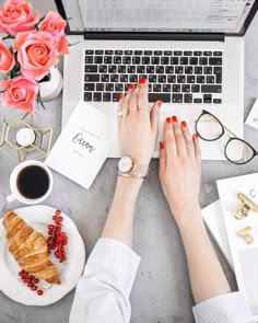 two hands typing on a laptop keyboard next to a plate with croissants