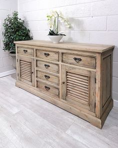 a large wooden dresser with shutter doors on the top and bottom, in front of a white brick wall