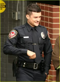 a smiling police officer in uniform walking down the street with his hand on his hip