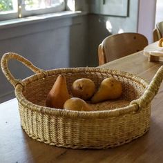 a wicker basket filled with pears sitting on top of a wooden dining table