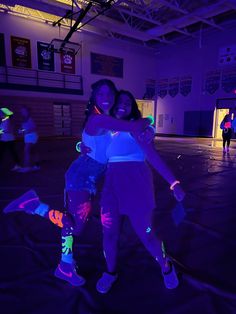 two young women hugging each other in an indoor gym area with neon lights on the floor