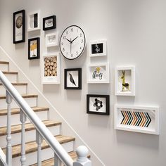 there are many framed pictures on the wall next to the stair case, which also has a clock