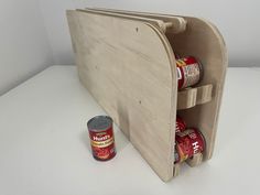 an open wooden magazine holder with cans of canned food in the bottom section and a can of canned drink next to it