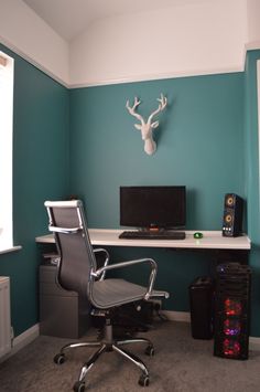 a desk with a chair, monitor and speakers in front of a deer head mounted on the wall