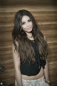 a woman with long hair standing in front of a wooden wall and posing for the camera