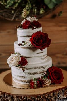 a three tiered wedding cake with red and white flowers on the top is sitting on a tree stump