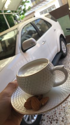 a person holding a cup and saucer with almonds in front of a car