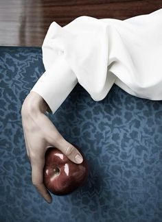 a person holding an apple on top of a blue carpeted floor in front of a wall