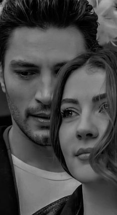 a black and white photo of a man and woman looking at each other with flowers in the background