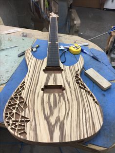 a wooden guitar sitting on top of a blue table covered in woodworking tools and materials