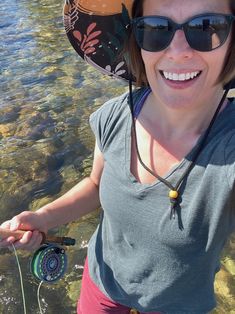 a woman standing in the water wearing a hat and holding a fishing rod with sunglasses on her head