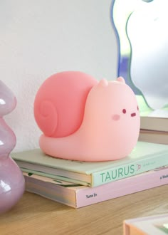 a pink snail lamp sitting on top of a stack of books next to a mirror