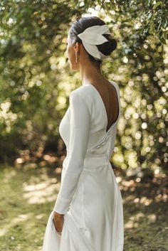 a woman wearing a white dress and feathered headpiece standing in front of trees