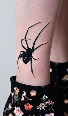 a black spider tattoo on the leg of a woman's legs with flowers all over it