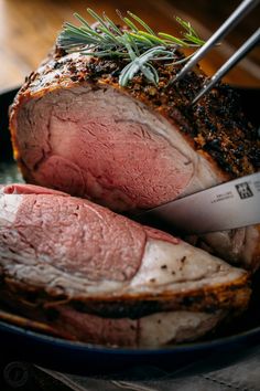 a piece of meat on a plate with a knife and some rosemary sprigs