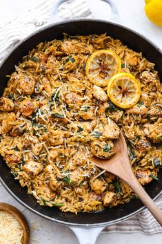 a skillet filled with chicken and rice next to lemons on a white table