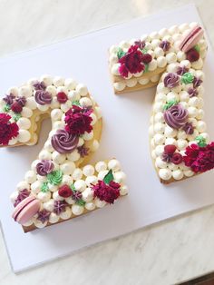 the number twenty seven decorated with flowers and icing on a white tray next to a marble counter top