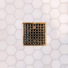 a white tiled wall with a gold metal grate in the middle and hexagonal tiles behind it