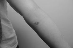 a small saturn tattoo on the left inner arm, with an arrow at the center