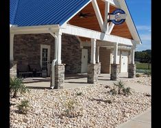 a small building with a blue roof and white trim on the front door is surrounded by rocks