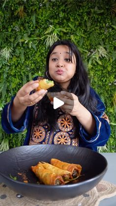 a woman eating food from a black bowl on top of a table next to a green wall