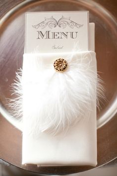 a white napkin with a gold brooch on it and a menu in the background