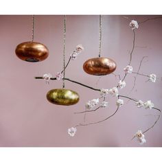 three metal ornaments hanging from a branch with white flowers in front of a pink wall